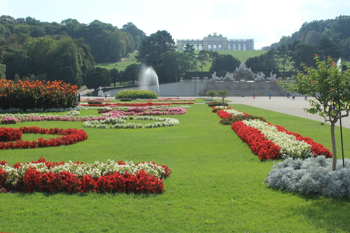 Blumenbeete in Rot, Weiß und Rosa über das Große Parterre hinweg, mit dem Neptunbrunnen und der Glorietten-Kolonnade auf dem Hügel dahinter